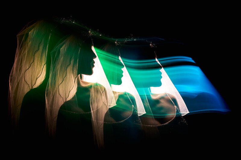 Silhouetted profile of a woman's head facing left with flowing hair, overlaid with gradient-lit geometric shapes transitioning from green to blue against black background.
