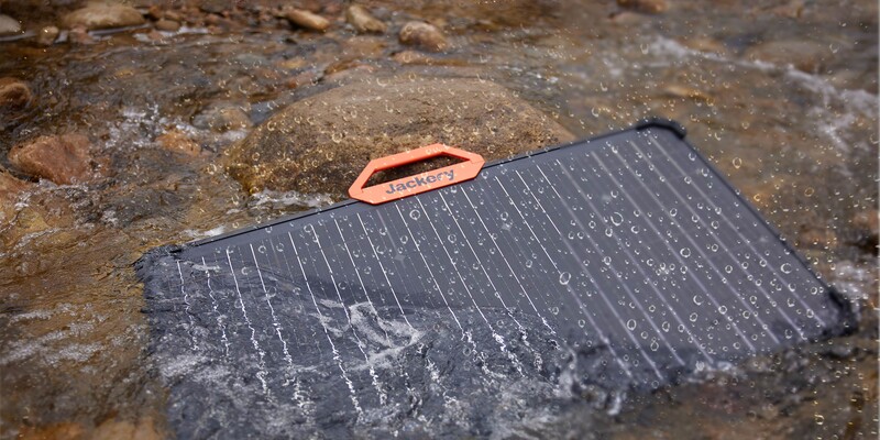 Waterlogged smartphone displaying water droplets on its dark screen next to an orange stylus on wet ground.
