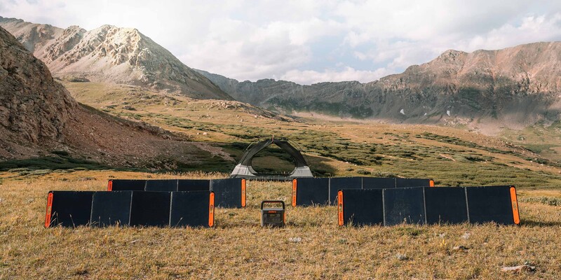 Solar panels arranged in a valley between mountains with a white tent and old truck nearby.