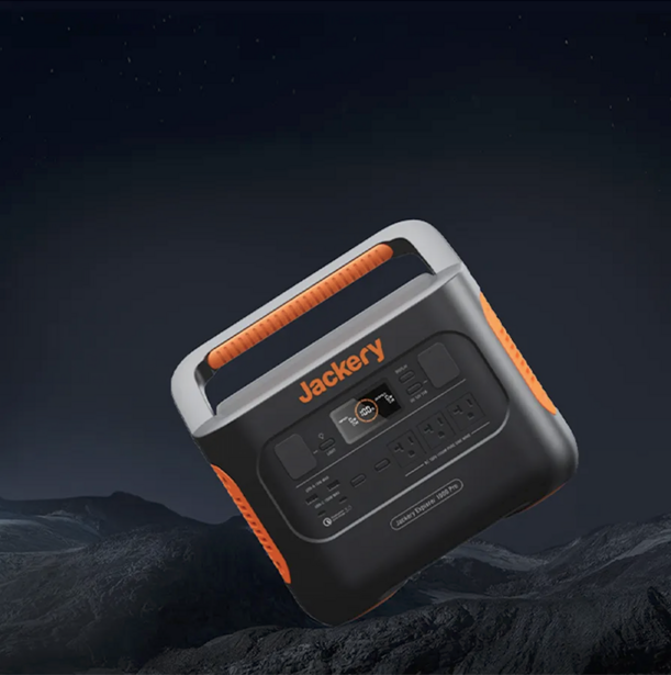 Portable power station with orange and black design displayed on rocky surface against dark sky.