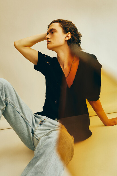 Woman in black short-sleeved shirt and light jeans posing against a two-tone background.
