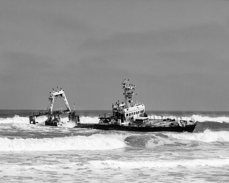 Industrial vessel operating in rough surf with large waves breaking around its hull.