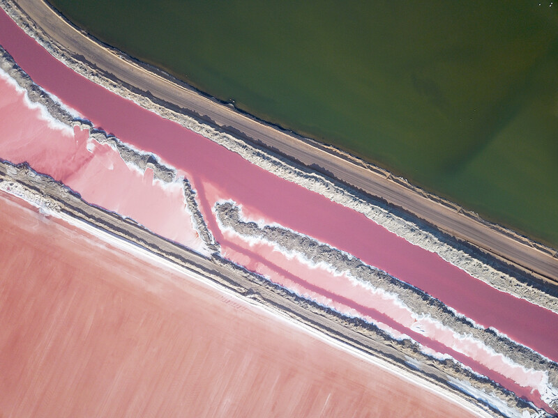 Aerial view of salt ponds with vibrant pink and green water separated by earthen berms.