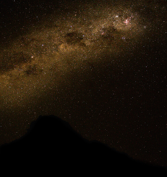 Milky Way galaxy stretching across night sky above a dark mountain silhouette.