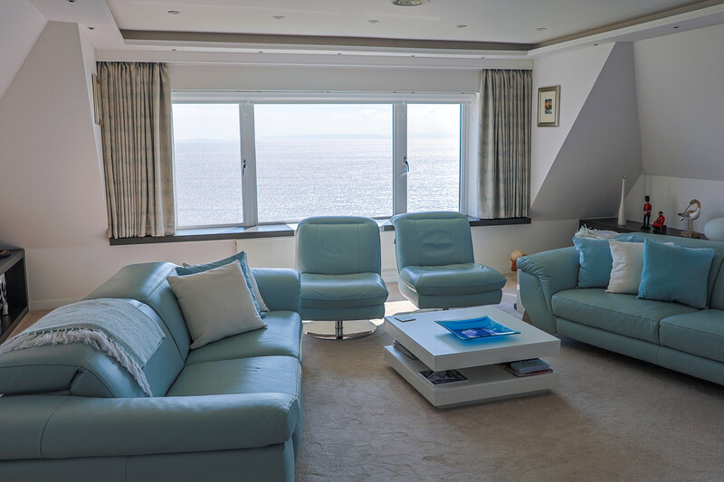 Luxurious modern living room with coordinated turquoise seating, ocean view windows, and neutral palette.