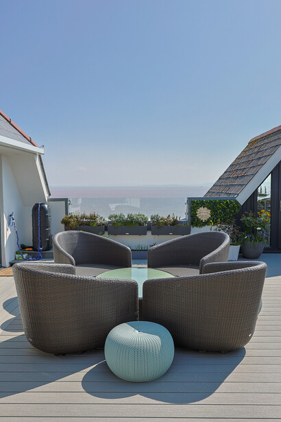 Modern lounge furniture arrangement on an elevated deck with pool and coastal view in background.