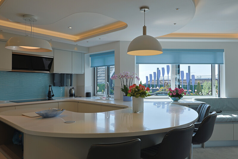Modern kitchen with curved island, turquoise backsplash, and city skyline view through floor-to-ceiling windows.