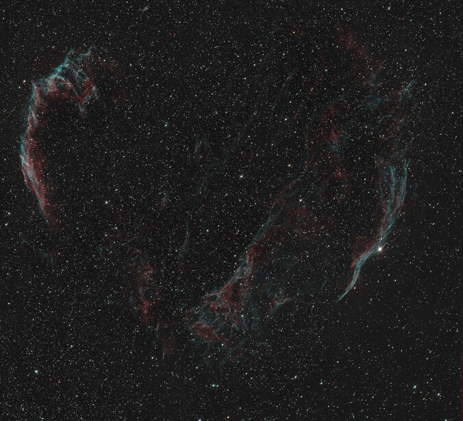Veil Nebula supernova remnant showing intricate filamentary structures in red and cyan against a starfield.