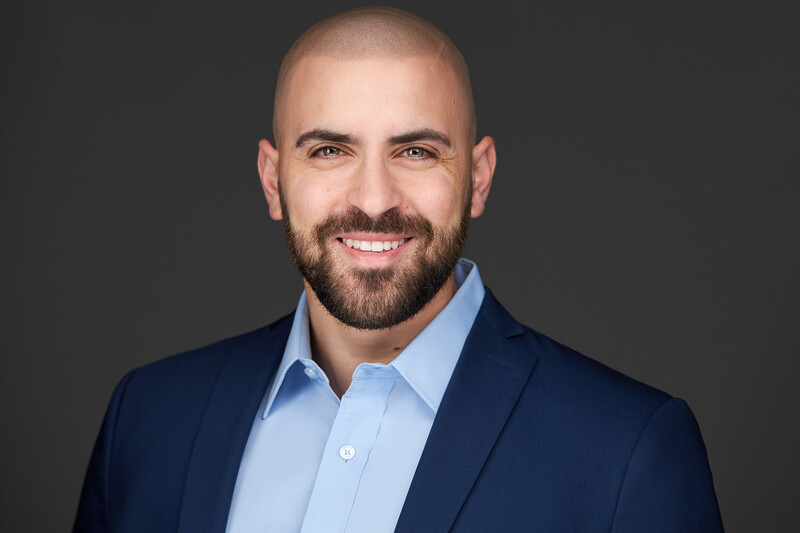 Professional headshot of a man with a beard wearing a dark blue blazer and light blue dress shirt.