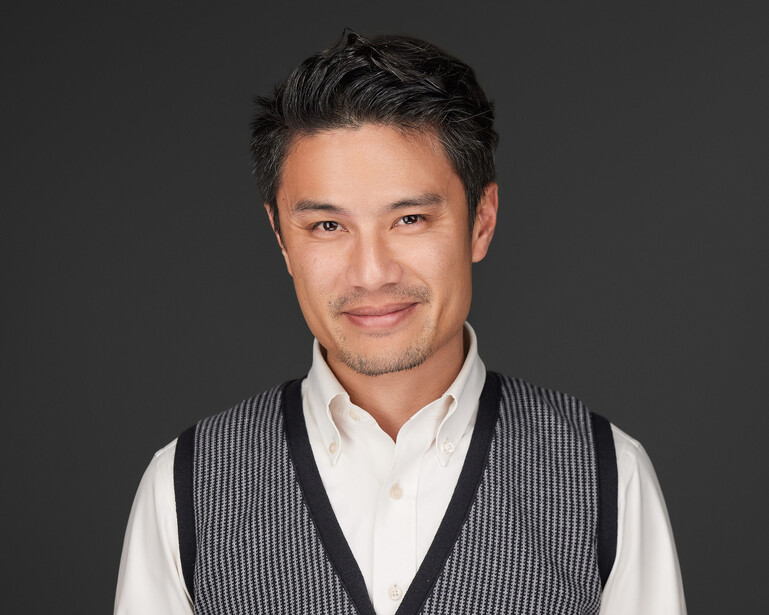 Professional headshot of a man wearing a white dress shirt and striped gray vest against a neutral gray backdrop.