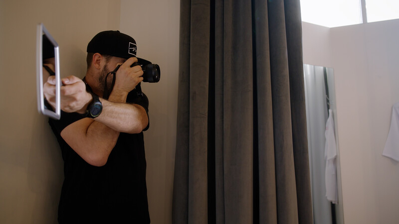 Photographer holding a camera to his face while framing a shot indoors.