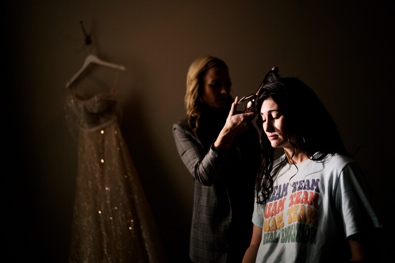 Photographer holding vintage camera photographing woman wearing graphic t-shirt against dark backdrop with dress form visible.