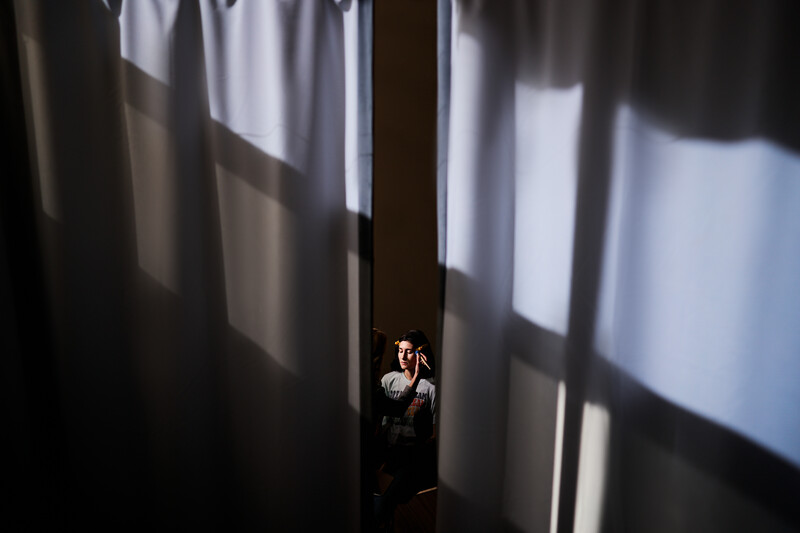 Person standing in narrow gap between large white fabric panels with dramatic window light creating geometric shadows.