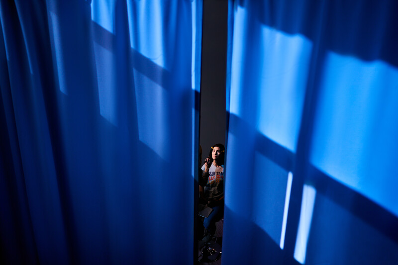 Solitary figure standing between tall blue-lit walls creating geometric patterns of light and shadow.