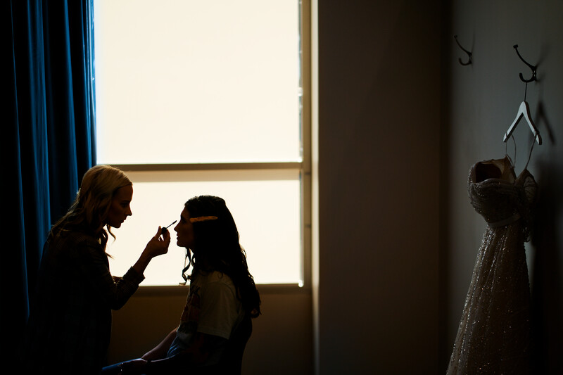 Silhouetted makeup artist applying makeup to a person's face against bright backlighting from a window.