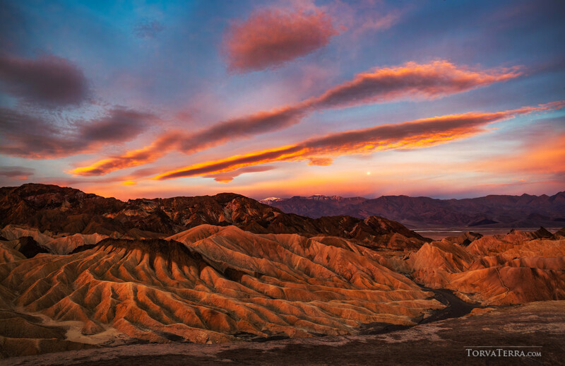 Dramatic sunset over layered desert mountains with golden and orange light illuminating eroded ridges.