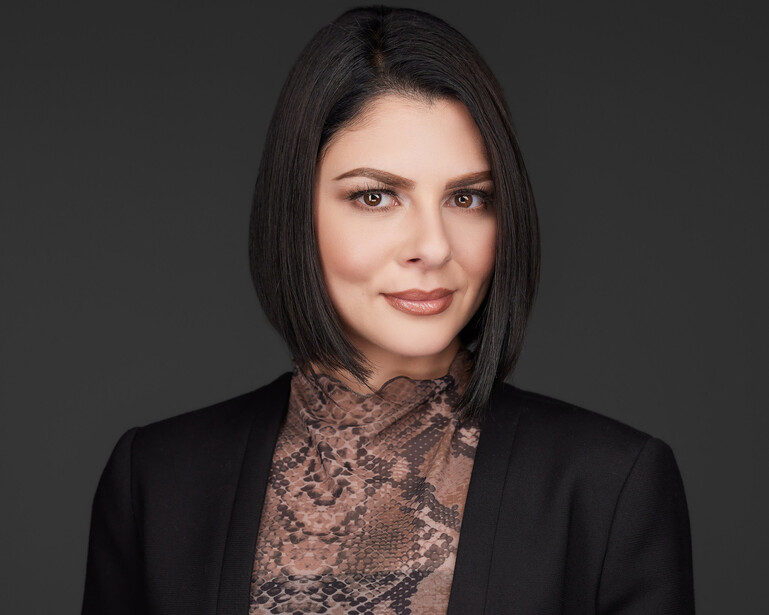 Professional headshot of a woman with dark hair wearing a black blazer over a patterned blouse.
