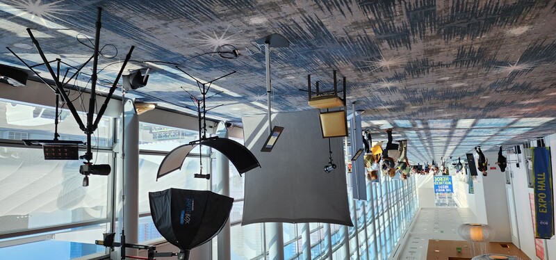 Professional photography studio setup with softbox lighting and reflectors in a modern convention center corridor.