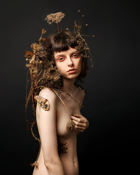 Nude woman covered in branches and moths