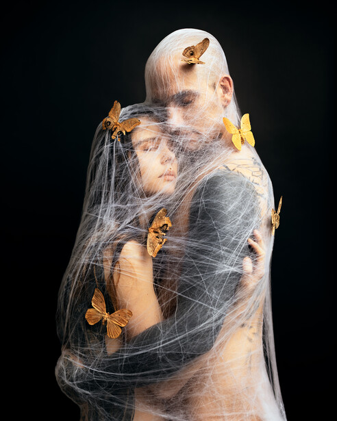 Couple embracing while covered in webs and moths.