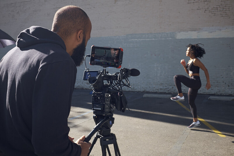 Cinematographer operating a professional camera on tripod while filming a runner in athletic gear on an urban rooftop.