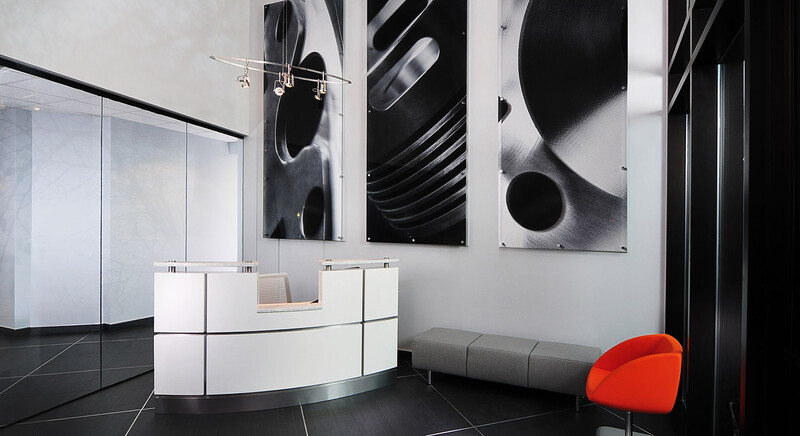 Modern interior space with monochromatic abstract wall art, curved reception desk, and vibrant red accent chair.