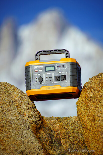 Portable power station balanced on rocky outcrop against blue sky with white clouds.