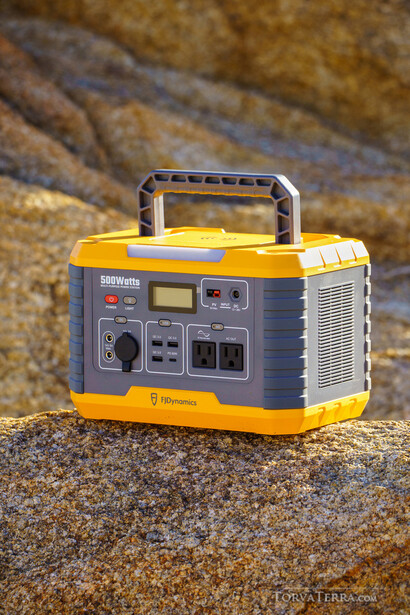 Yellow and blue portable power station with carrying handle on rocky ground.