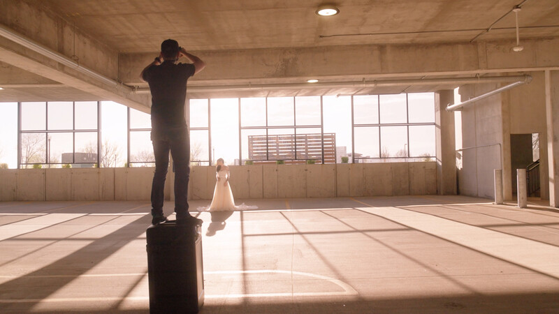 Man in silhouette standing on a pillar in an empty warehouse space with large windows and dramatic sunlight casting long shadows.