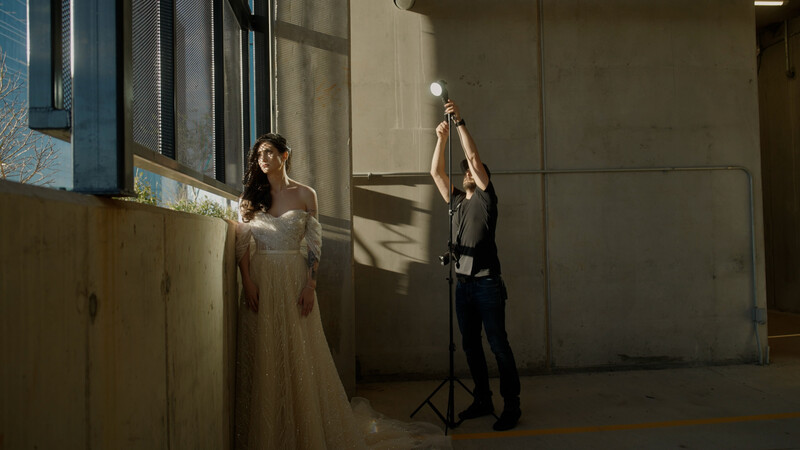 Studio portrait session with off-camera flash lighting a woman in an elegant white dress while photographer adjusts equipment.