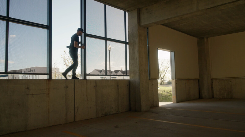 Person in business attire leaning against large window in empty concrete interior space.