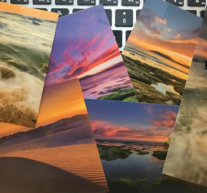Collection of landscape photography prints spread across a keyboard showing sunset and golden hour scenes.