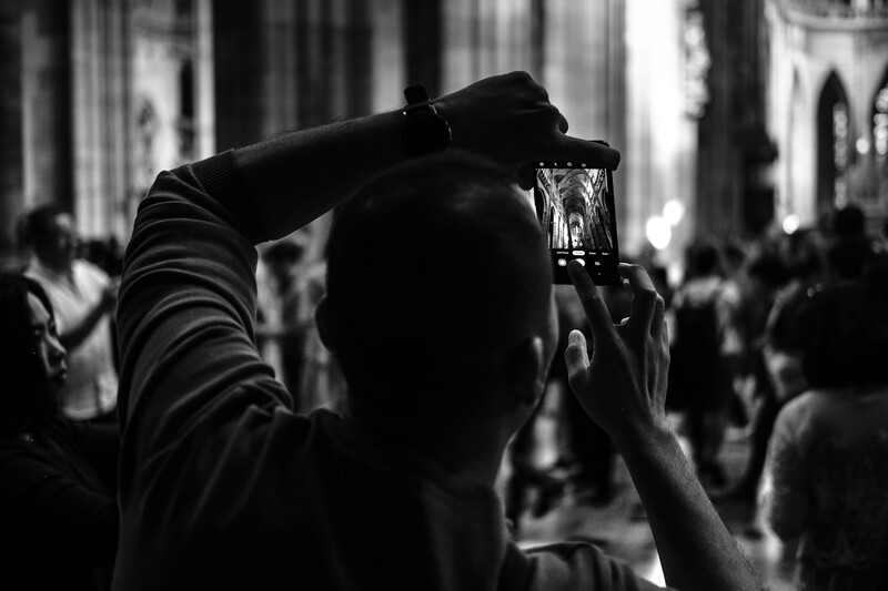 Person holding smartphone above their head to photograph a crowded urban street scene.