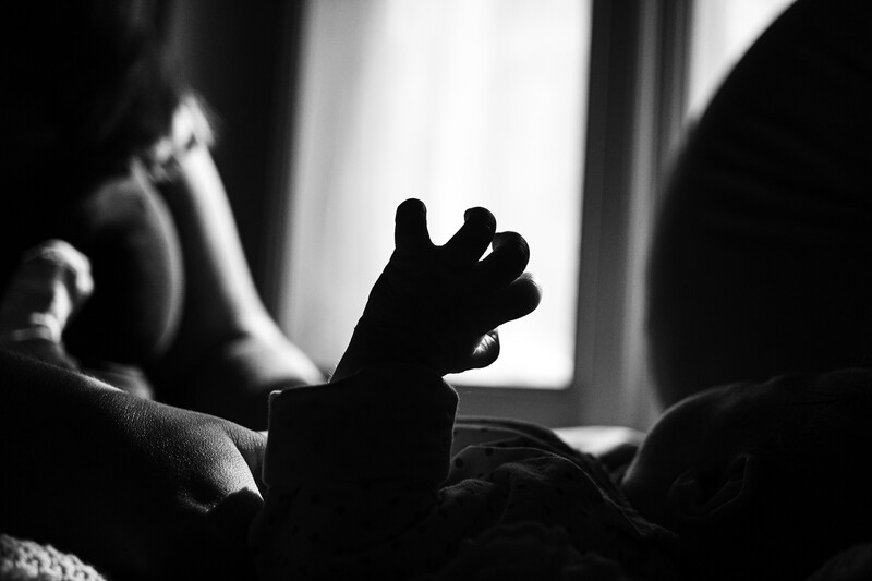 Silhouetted baby's hand reaching upward toward bright window light in high-contrast black and white photography.