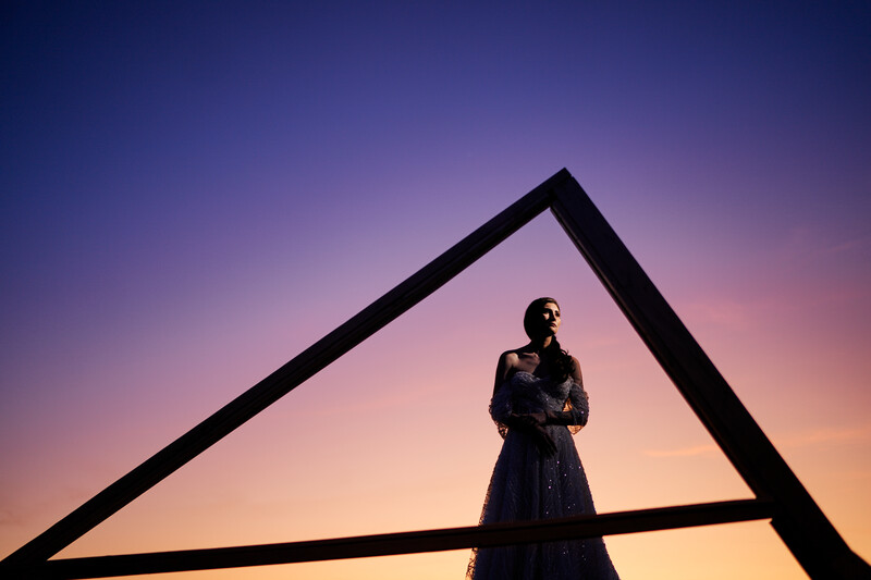 Silhouetted figure standing within a geometric triangular frame against a twilight sky.
