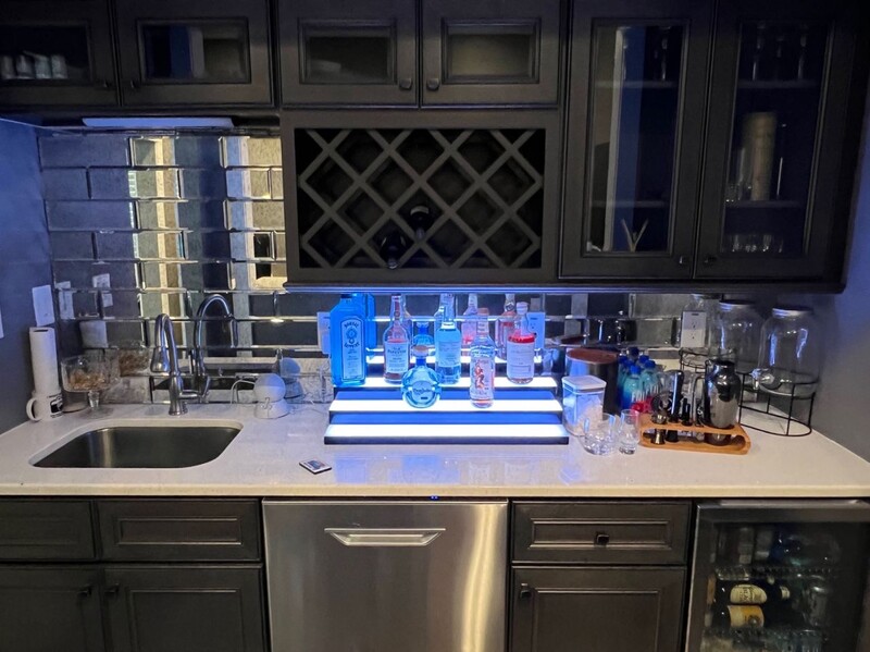 Modern kitchen counter illuminated by blue LED lighting with product displays and glassware.