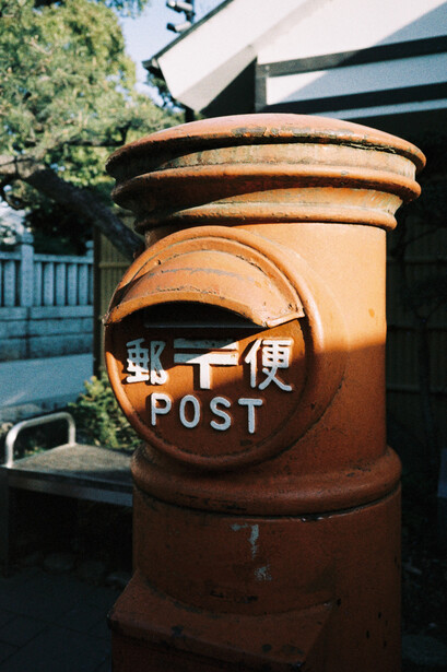 Rusty vintage mailbox with Japanese characters and mail slot, photographed outdoors in daylight.