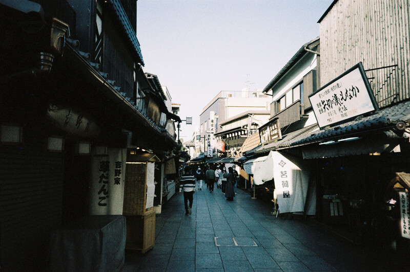 Narrow pedestrian alley lined with traditional wooden buildings and shop signs in soft afternoon light.