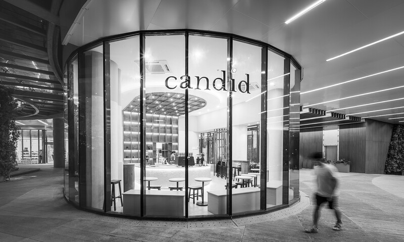 Curved glass storefront with black framing and blurred figure walking past in modern interior space.
