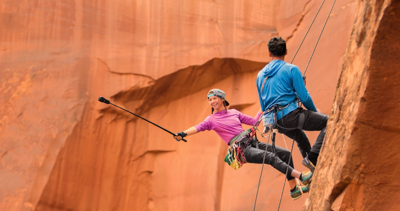 Two climbers rappelling down a massive sandstone cliff face in bright sunlight.
