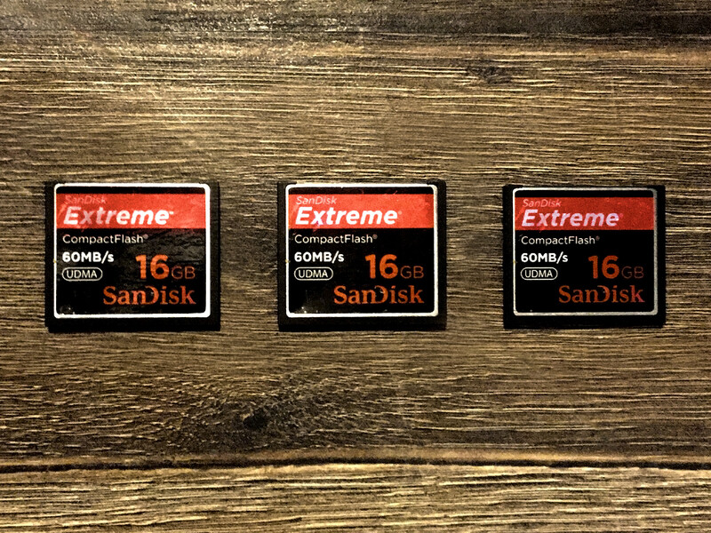 Three SanDisk Extreme CompactFlash cards with 16GB capacity rated at 60MB/s displayed on a wooden surface.