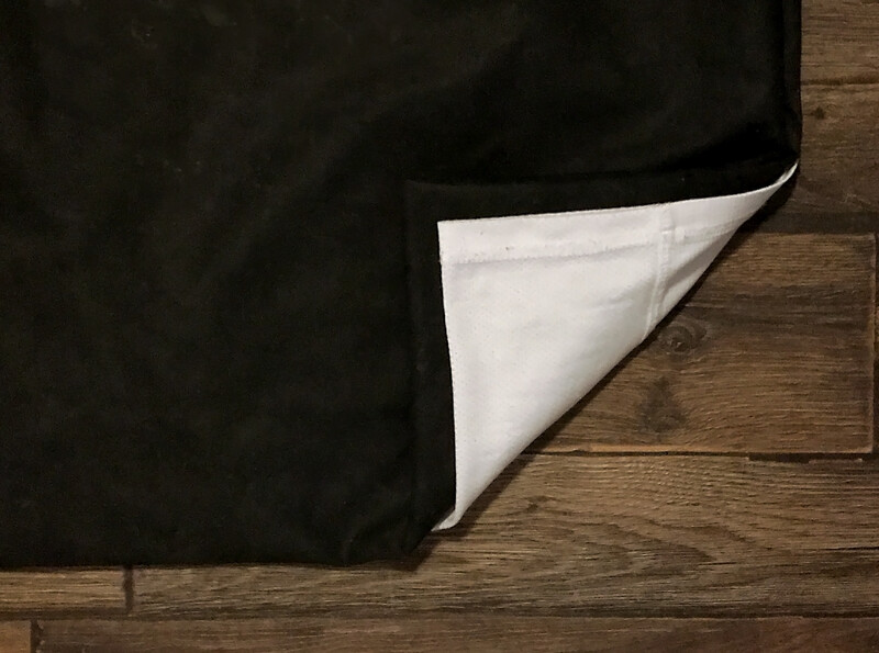 Black fabric with white lining peeled back corner on wooden floor.