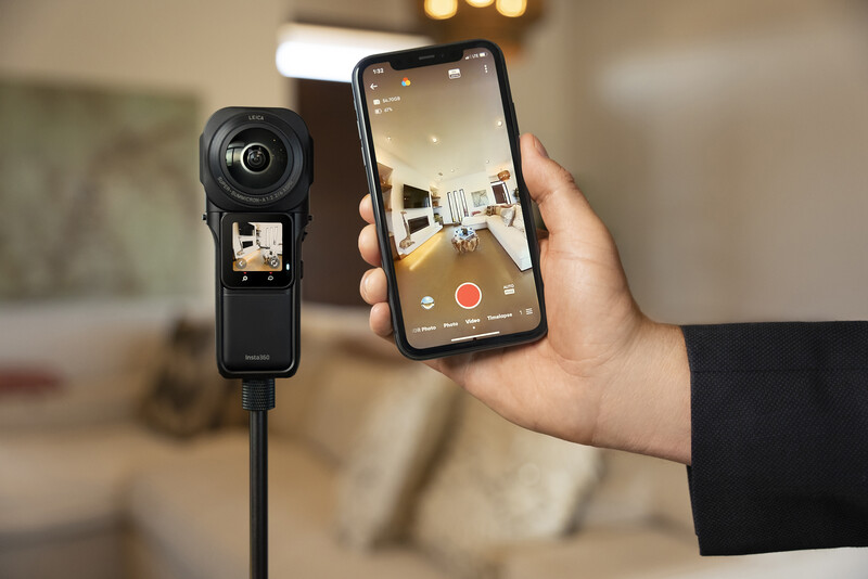 Hand holding smartphone displaying live video feed from a compact action camera mounted on a tripod.