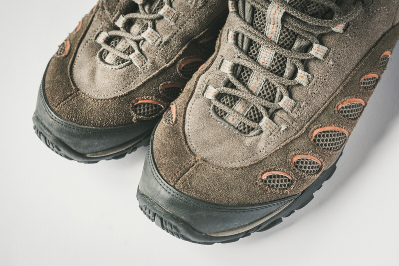Pair of worn hiking boots with tan suede uppers and dark rubber soles, photographed from above against a light gray background.