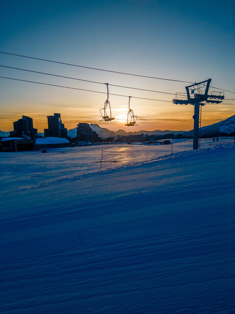 Snow-covered landscape at dusk with utility poles and distant industrial structures silhouetted against a blue-orange sky.