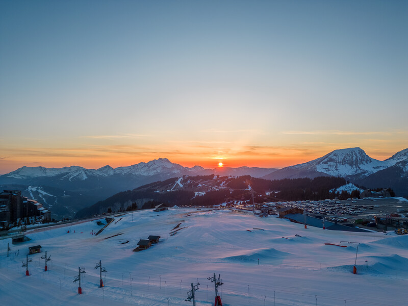 Snowy ski resort at sunrise with distant mountains and lifts in winter light.