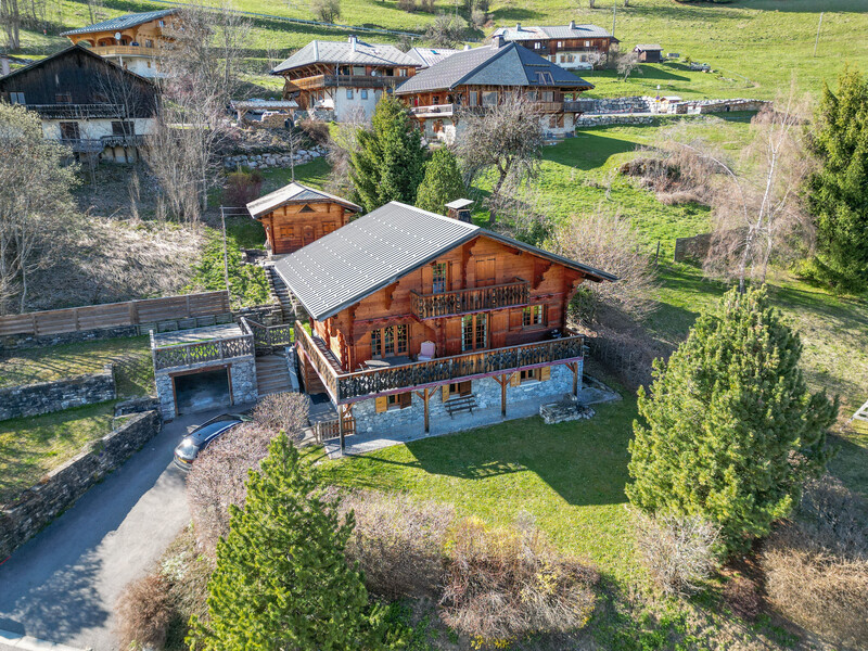 Aerial view of a modern wooden lodge surrounded by green fields and bare trees in spring.