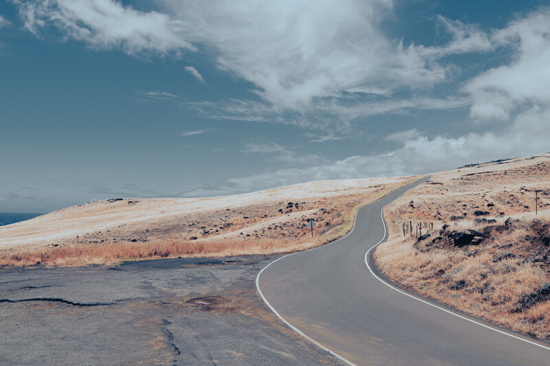 Curved asphalt road winding through arid, sparse terrain with mountains and blue sky.