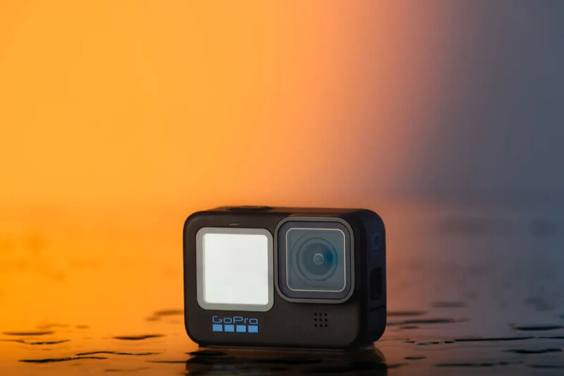 GoPro Hero 11 action camera positioned on a reflective surface against a warm golden-hour gradient backdrop.