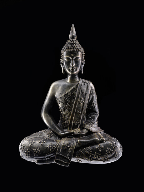 Monochromatic sculpture of a seated Buddha figure with ornate crown and draped robes against black background.